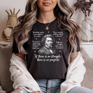 May include: Black t-shirt featuring a portrait of Frederick Douglass with quotes about knowledge and struggle. The shirt includes the text "If there is no struggle, there is no progress."