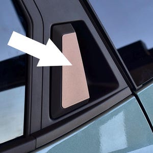 Könnte beinhalten: Nahaufnahme eines Innendetails eines Autos. Ein rechteckiges, metallfarbenes Akzentstück ist in einen schwarzen Rahmen eingesetzt, wahrscheinlich Teil eines Türgriffs oder einer Zierleiste. Der umliegende Bereich ist in einem gedämpften Türkis gehalten.
