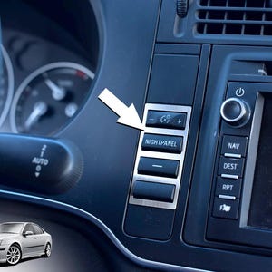 May include: Close-up of a car dashboard with a focus on the "NIGHTPANEL" button. The button is part of a panel with other buttons and a screen. The car is silver.