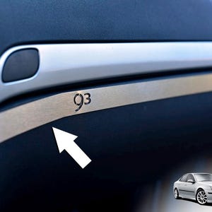 Könnte beinhalten: Detail des Fahrzeuginnenraums. Ein Zierleiste aus gebürstetem Metall mit der Zahl "93" ist zu sehen. Das Armaturenbrett ist dunkelblau mit silberfarbenen Akzenten. Ein silbernes Auto befindet sich in der unteren rechten Ecke.