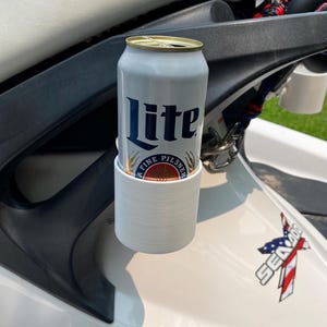 May include: A white and silver Miller Lite beer can in a white cup holder, mounted on a white Sea-Doo watercraft. The can has the words "Lite" and "Fine Pilsner" printed on it. The watercraft has a red, white, and blue graphic.