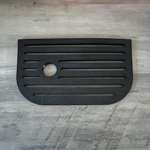 May include: A black, rectangular vent cover with horizontal slots and a circular opening. The cover has rounded corners and is made of a matte black material. The design is simple and functional.