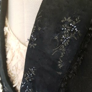 May include: Black fabric with a floral pattern and beaded accents. The fabric has a frayed edge.