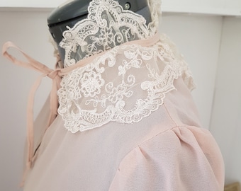 May include: A pale pink blouse with a delicate lace collar. The collar is a ruffled design with a white lace trim.