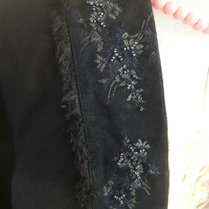 May include: Black velvet jacket with a fringed trim and floral embroidery accented with black beads.