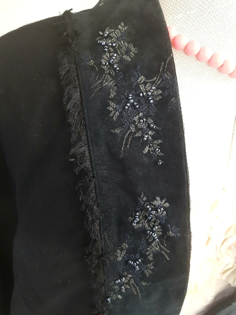 May include: Black velvet jacket with a fringed trim and floral embroidery accented with black beads.