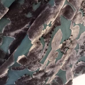 May include: Close-up of a dark green fabric with a black velvet floral pattern and black beads.
