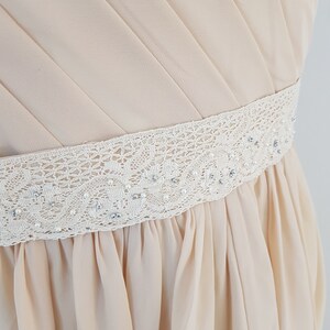 May include: A light beige dress with a white lace and pearl trim around the waist.