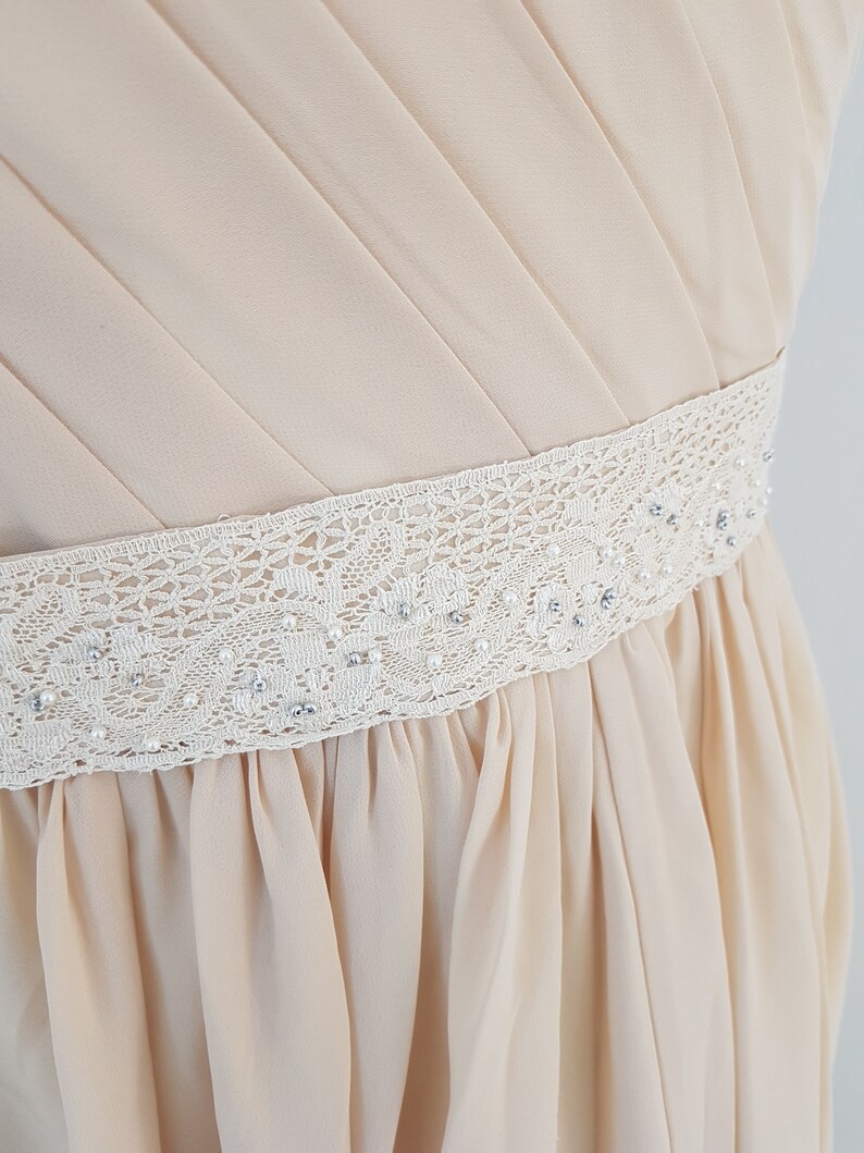 May include: A light beige dress with a white lace and pearl trim around the waist.