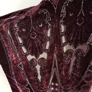 May include: A burgundy velvet shawl with a paisley pattern and silver embellishments. The shawl is sheer and has a delicate, flowing design.