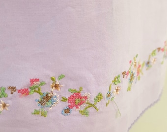 May include: A lavender fabric with a delicate floral embroidery design. The embroidery features small pink, blue, and green flowers with brown centers.