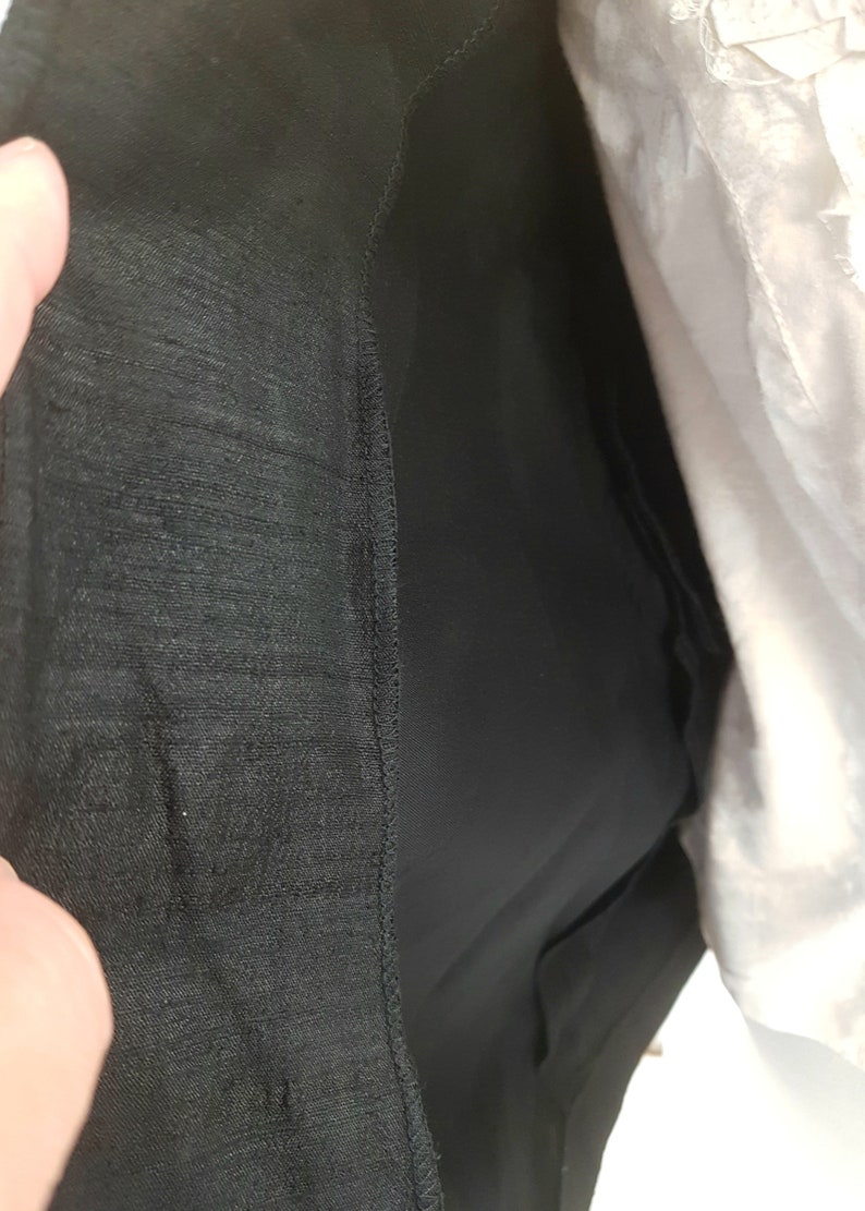 May include: Close-up of the inside of a black skirt with a lining. The lining is a smooth, silky fabric.