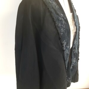 May include: A black cape with a beaded trim around the collar and down the front. The trim is made of small black beads and sequins.