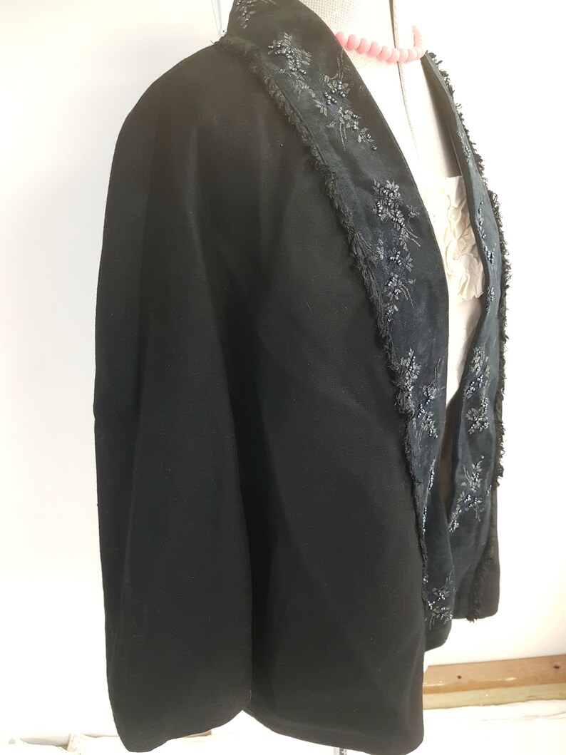 May include: A black cape with a beaded trim around the collar and down the front. The trim is made of small black beads and sequins.
