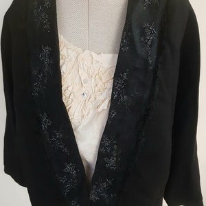 May include: A black velvet jacket with a satin collar and beaded trim. The jacket has a shawl collar and a long, flowing silhouette.