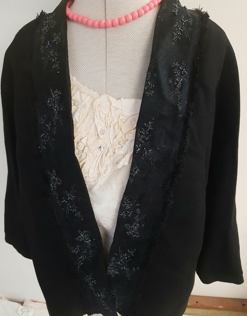 May include: A black velvet jacket with a satin collar and beaded trim. The jacket has a shawl collar and a long, flowing silhouette.