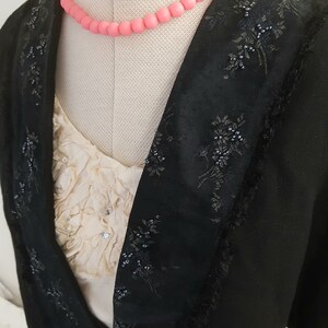 May include: A black blazer with a beaded floral design and a pink beaded necklace.