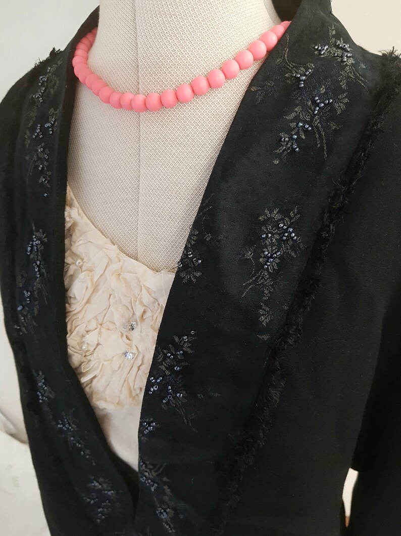 May include: A black blazer with a beaded floral design and a pink beaded necklace.