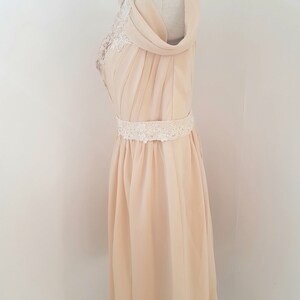May include: A pale yellow chiffon dress with a lace overlay on the bodice and a lace belt. The dress has a draped neckline and a flowing skirt.