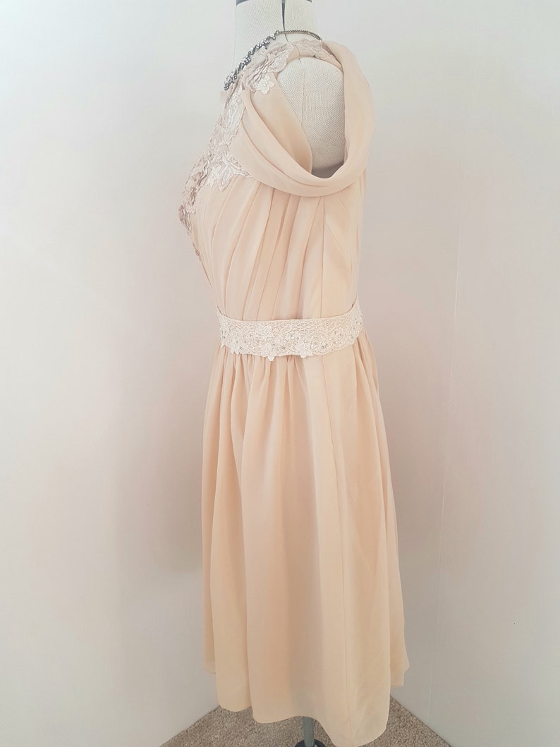May include: A pale yellow chiffon dress with a lace overlay on the bodice and a lace belt. The dress has a draped neckline and a flowing skirt.
