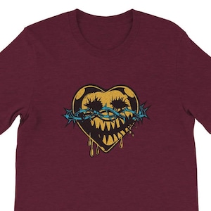 May include: Burgundy t-shirt featuring a distressed graphic of a heart with a menacing face, a crown of thorns, and dripping details. The heart is yellow with black accents, and the thorns are blue. A unique design for a casual tee.