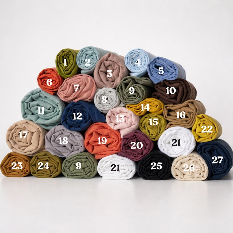 K&ouml;nnte beinhalten: Eine Sammlung gerollter Stoffe in verschiedenen Farben, darunter Blau-, Gr&uuml;n-, Rosa- und Gelbt&ouml;ne. Die Rollen sind von 1 bis 27 nummeriert und pyramidenf&ouml;rmig angeordnet. Der Stoff scheint Leinen oder ein &auml;hnliches Naturmaterial zu sein.