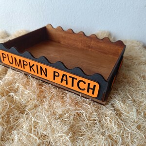 May include: Wooden Pumpkin Patch sign with a scalloped edge. The sign has a dark brown interior and black trim. The words "PUMPKIN PATCH" are in black letters on an orange background. The sign is sitting on a bed of straw.