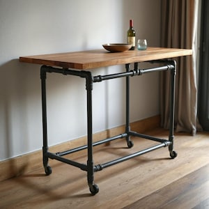 May include: A wooden table with a black metal frame and wheels. The table has a natural wood finish and is supported by black metal pipes. The table is on a wooden floor.