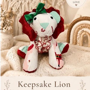May include: A handmade Keepsake Lion made from baby clothes. The lion has a white face with a green bow, red mane, and mint green ears. The lion's body is decorated with a Santa Claus pattern. The text "Handmade with Love" is visible.