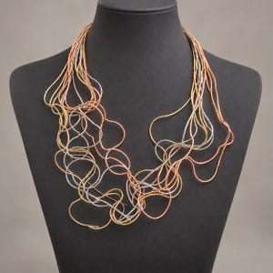 May include: A multi-strand statement necklace featuring thin, flexible wire loops in alternating metallic tones of copper, gold, and silver. The design consists of numerous interconnected, organic circular shapes that drape across the chest area.