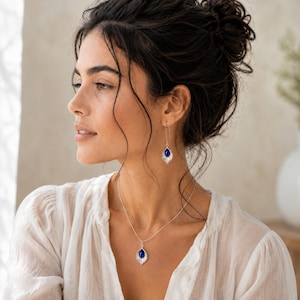 May include: A silver necklace and matching drop earrings featuring a teardrop-shaped deep blue stone set within a textured silver leaf-shaped frame. The jewellery set includes a delicate silver chain and thin silver ear wires for a refined look.