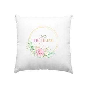 Könnte beinhalten: Weißes quadratisches Kissen mit floralem Design. Das Design zeigt einen goldenen Kreis mit den Worten "hallo FRÜHLING" in einem Farbverlauf aus Rosa, Gelb und Grün. Rosa und weiße Blumen und grüne Blätter umgeben den Kreis.