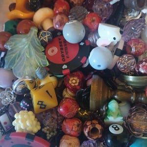 May include: A selection of beads and charms in various shapes and colours. Includes a yellow die, a red and black poker chip with text, a white bunny, and a black eight ball.