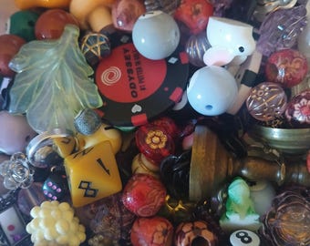 May include: A collection of various beads and charms in different shapes, sizes, and colors. Includes a yellow die, a red and black poker chip with text, a white bunny, and a black eight ball.