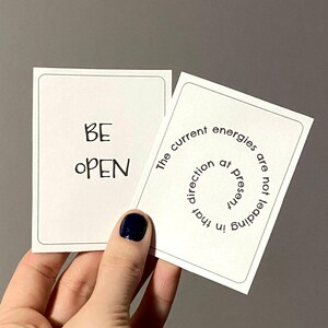 May include: Two white cards with black text. The first card says "BE OPEN". The second card says "The current energies are not leading in that direction at present".