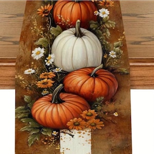 May include: A fall-themed table runner featuring a still life of pumpkins and flowers. The runner showcases three orange pumpkins and one white pumpkin, surrounded by daisies and orange flowers. The background is a warm brown.