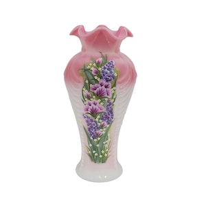 Peut inclure: Un vase en céramique rose et blanc avec un bord festonné. Le vase est décoré d'un motif floral avec des fleurs violettes et lavande et des feuilles vertes. Le vase a une base évasée.