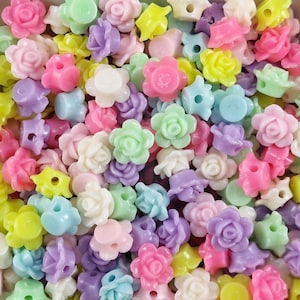 Könnte beinhalten: Eine Sammlung von pastellfarbenen Plastikrosenperlen. Die Perlen sind in verschiedenen Schattierungen von Rosa, Lila, Blau, Grün und Gelb. Sie haben alle die Form einer Rose mit einem kleinen Loch in der Mitte zum Auf fädeln.