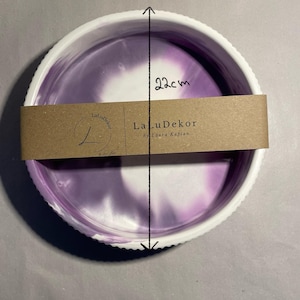Op de afbeelding: Een ronde decoratieve schaal met een witte, geschulpte rand en een paars en wit gemarmerd interieur. De schaal heeft een diameter van 22 cm. Een bruine papieren band met de tekst "LaLuDekor by Laura Kaplan" is om de schaal gewikkeld.