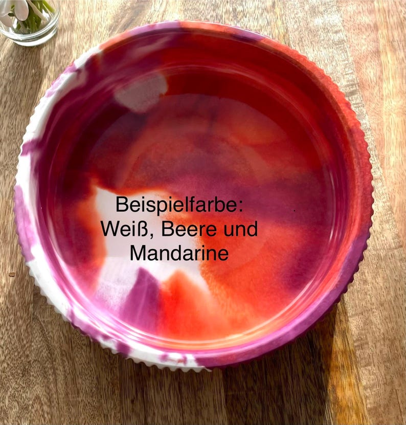 Op de afbeelding: Een ronde, decoratieve kom met een getextureerde rand. De binnenkant heeft een mix van wit, bes en mandarijnkleuren. De tekst "Beispielfarbe: Wei&szlig;, Beere und Mandarine" is zichtbaar op de kom.