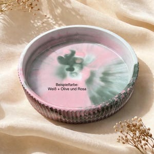 Op de afbeelding: Een ronde decoratieve tray met een geribbelde rand. De binnenkant heeft een werveling van roze, witte en groene kleuren. De tekst "Beispielfarbe: Wei&szlig; + Olive und Rosa" is zichtbaar op de tray.