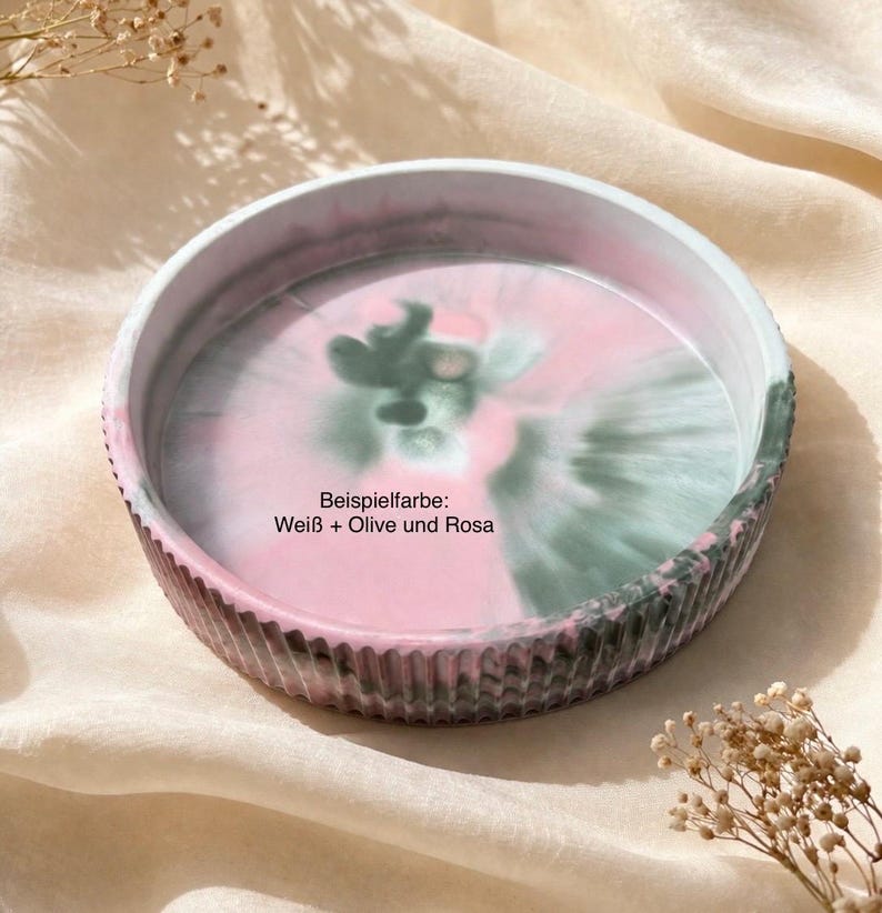 Op de afbeelding: Een ronde decoratieve tray met een geribbelde rand. De binnenkant heeft een werveling van roze, witte en groene kleuren. De tekst "Beispielfarbe: Wei&szlig; + Olive und Rosa" is zichtbaar op de tray.
