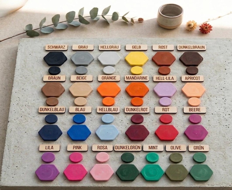 Op de afbeelding: Een kleurenpalet met zeshoekige en cirkelvormige objecten in verschillende kleuren. Elke kleur is gelabeld met een houten label. Kleuren zijn onder meer zwart, grijs, geel, oranje, rood en groen.