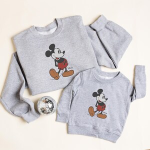 Pu&ograve; includere: Due felpe grigie con una grafica classica di Topolino. La felpa pi&ugrave; grande ha le maniche lunghe, mentre quella pi&ugrave; piccola &egrave; per bambini. Il design di Topolino include nero, rosso e marrone.