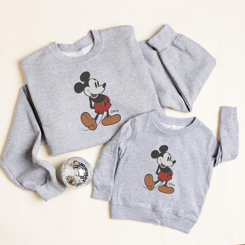 Pu&ograve; includere: Due felpe grigie con una grafica classica di Topolino. La felpa pi&ugrave; grande ha le maniche lunghe, mentre quella pi&ugrave; piccola &egrave; per bambini. Il design di Topolino include nero, rosso e marrone.