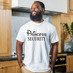 Puede incluir: Una camiseta blanca con un gr&aacute;fico negro que dice "Princess Security" en una fuente estilizada.