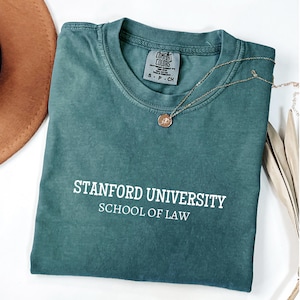May include: A dark green t-shirt with the text "Stanford University School of Law" in white lettering. The shirt is made of a soft, comfortable material and has a relaxed fit.