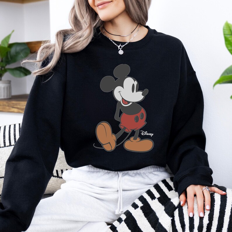 Pu&ograve; includere: Felpa nera con grafica di Topolino. Il personaggio dei cartoni animati &egrave; raffigurato nella sua posa classica, con pantaloncini rossi, scarpe marroni e guanti bianchi. Il logo Disney &egrave; stampato in basso a destra.