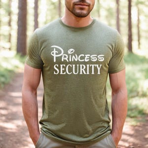 Puede incluir: Una camiseta verde con un gr&aacute;fico blanco que dice "Princess Security" con un logotipo de castillo de Disney estilizado.