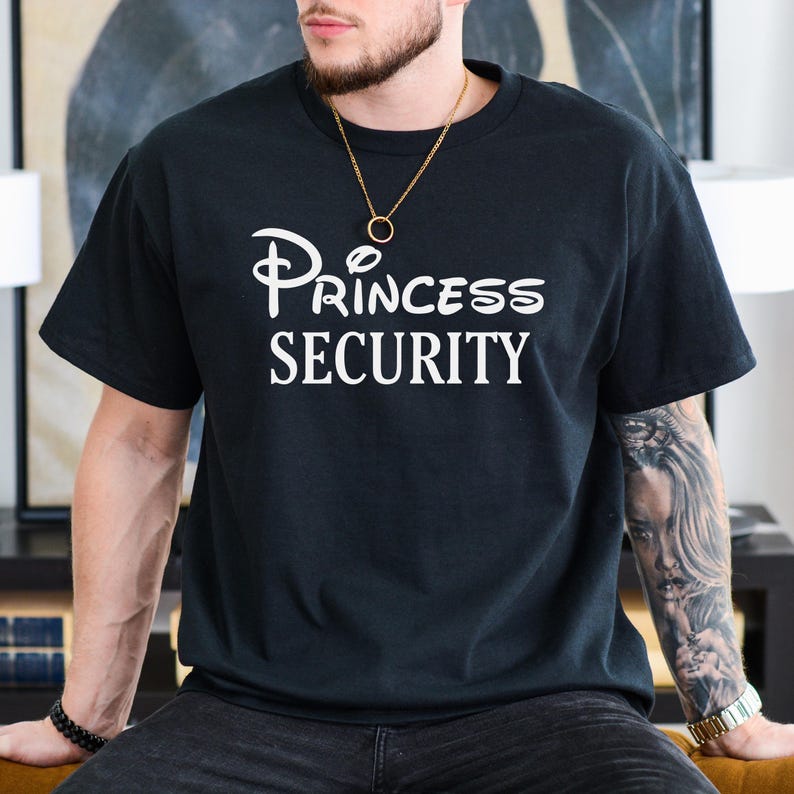Puede incluir: Una camiseta negra con un gr&aacute;fico blanco que dice "Princess Security" con un logotipo de castillo de Disney estilizado.